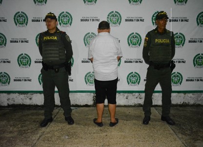 Esta persona tiene orden de captura con fines de extradicion Persona de espaldas y al lado de dos policias en foto