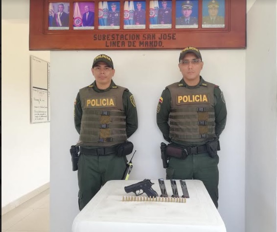 Incauta arma de fuego Dos policias frente a una arma de fuego puesta en una mesa