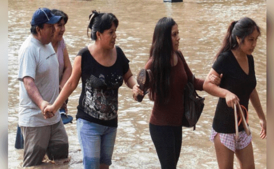 Personas pasando al lado de un rio formado por lluvias