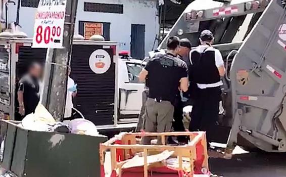 Foi encontrado dentro de um caminhão de lixo Pessoas em uma rua vendo um morto
